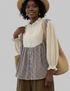 Woman wearing a checkered dress over a beige blouse with a straw bag on a plain background