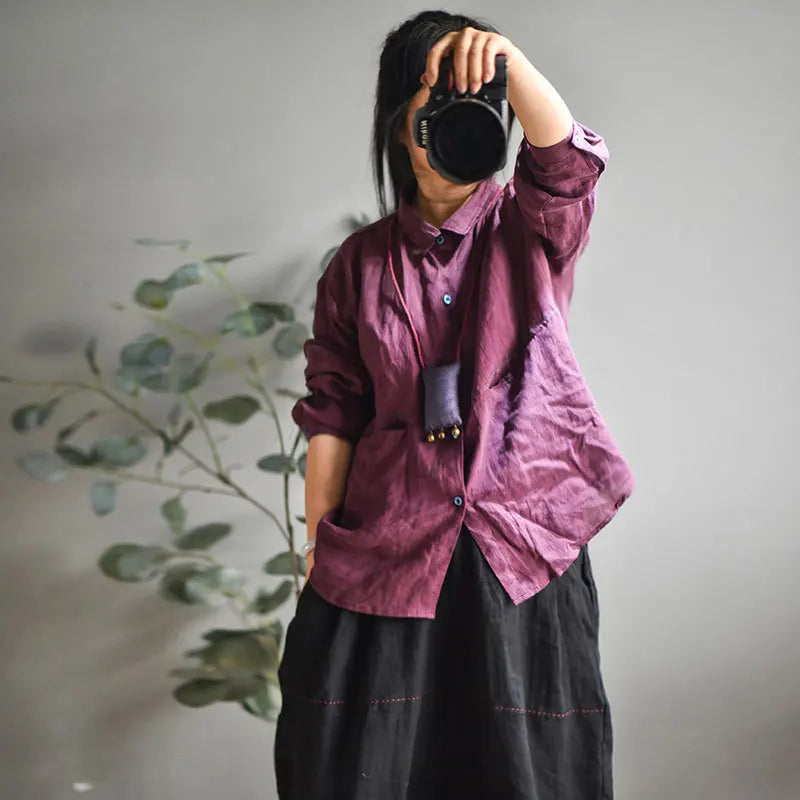 A person taking a mirror selfie wearing a wrinkled, deep plum-purple linen button-up shirt and a black skirt, holding a black camera in front of their face. A small black pouch hangs from the shirt&