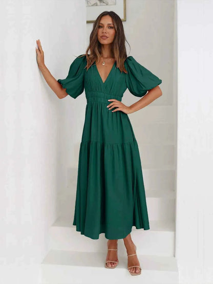 Woman in a green tiered midi dress with short puff sleeves and a surplice V-neck.