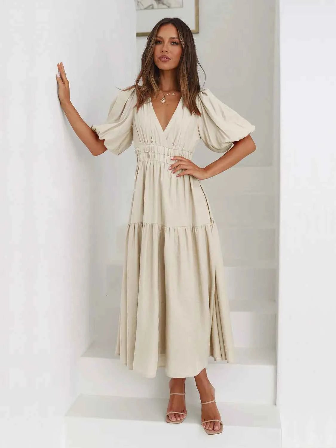 Woman in a beige tiered midi dress with short puff sleeves and a surplice V-neck.