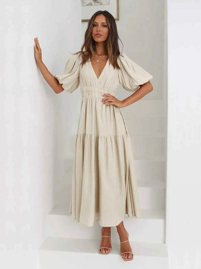 Woman in a beige tiered midi dress with short puff sleeves and a surplice V-neck.