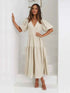 Woman in a beige tiered midi dress with short puff sleeves and a surplice V-neck.