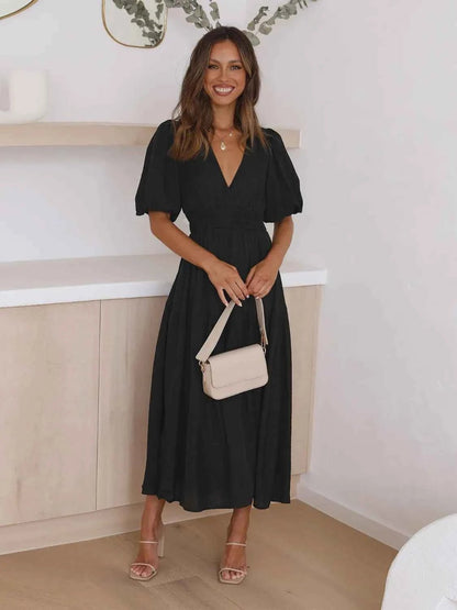Woman in a black tiered midi dress with short puff sleeves and a surplice V-neck.