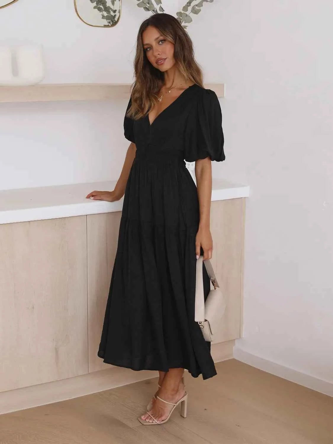 Woman in a black tiered midi dress with short puff sleeves and a surplice V-neck.