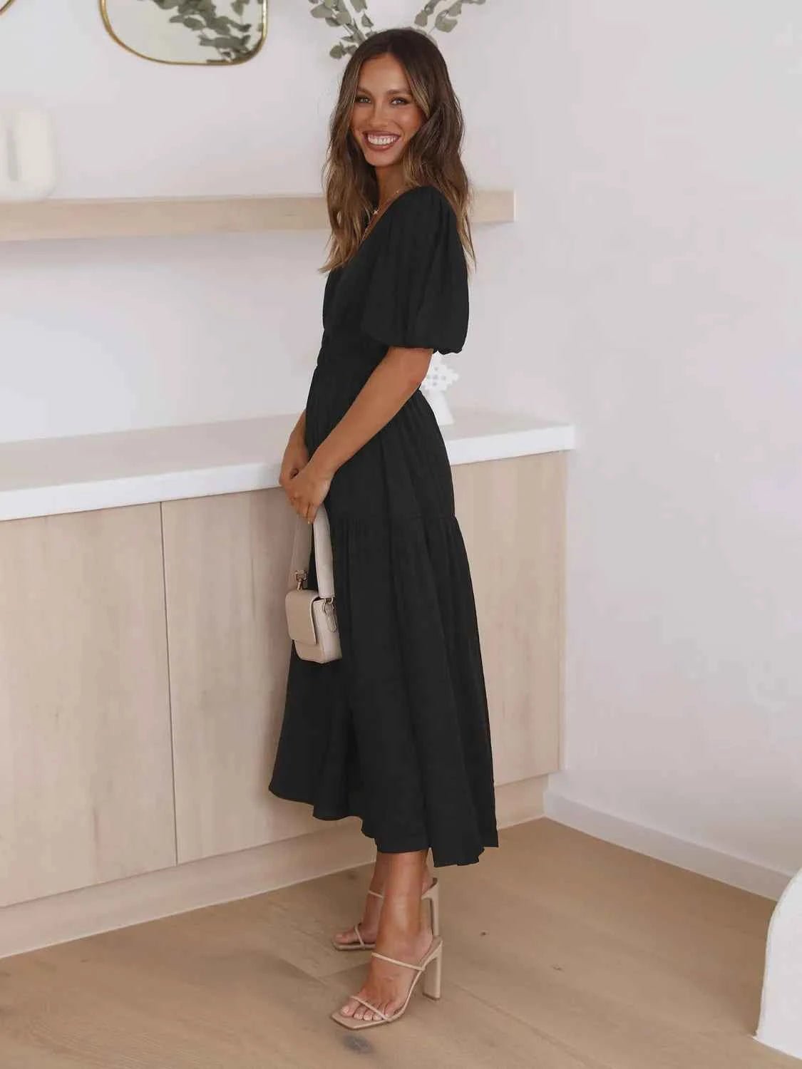 Woman in a black tiered midi dress with short puff sleeves and a surplice V-neck.