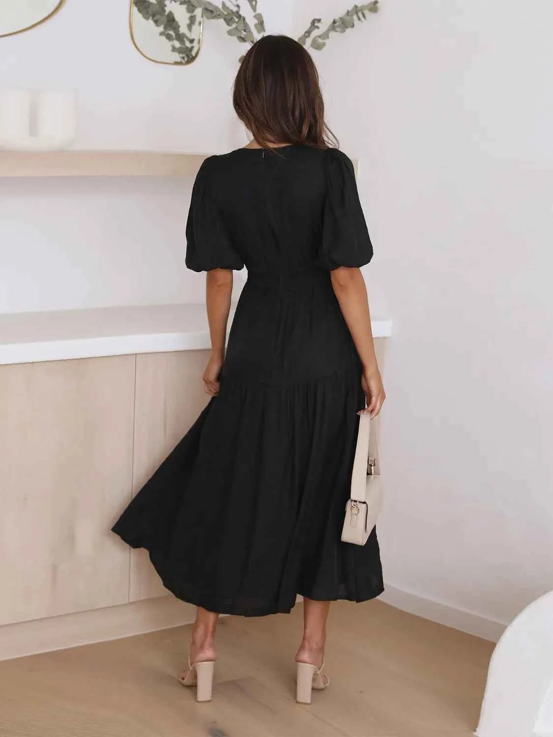 Woman in a black tiered midi dress with short puff sleeves and a surplice V-neck.