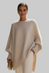 Woman wearing a beige poncho and holding a gold clutch against a neutral background