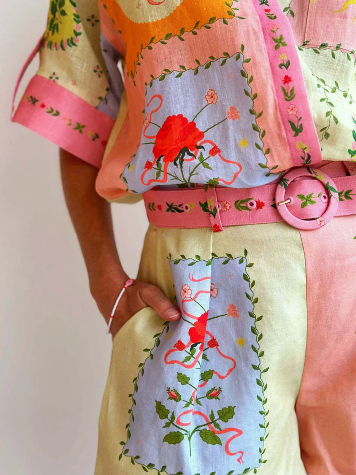 Colorful embroidered outfit with a pink belt on a plain background