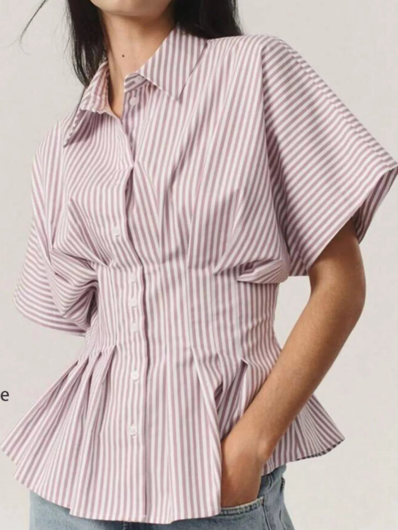 Person wearing a pink and white striped shirt with a peplum waist on a plain background
