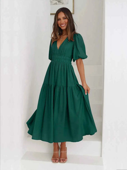 Woman in a green tiered midi dress with short puff sleeves and a surplice V-neck.