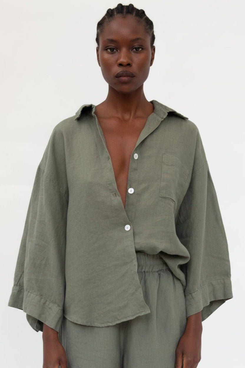 A model wearing an olive green linen button-down shirt with wide sleeves and matching trousers, photographed against a plain white studio background.