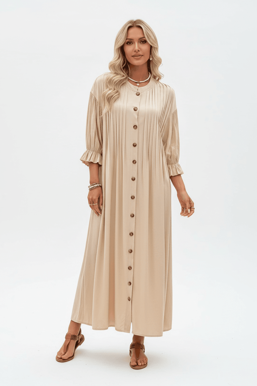 A woman modeling a beige midi-length pleated dress with three-quarter ruffled sleeves and a front button closure, paired with brown sandals, against a plain white studio background.