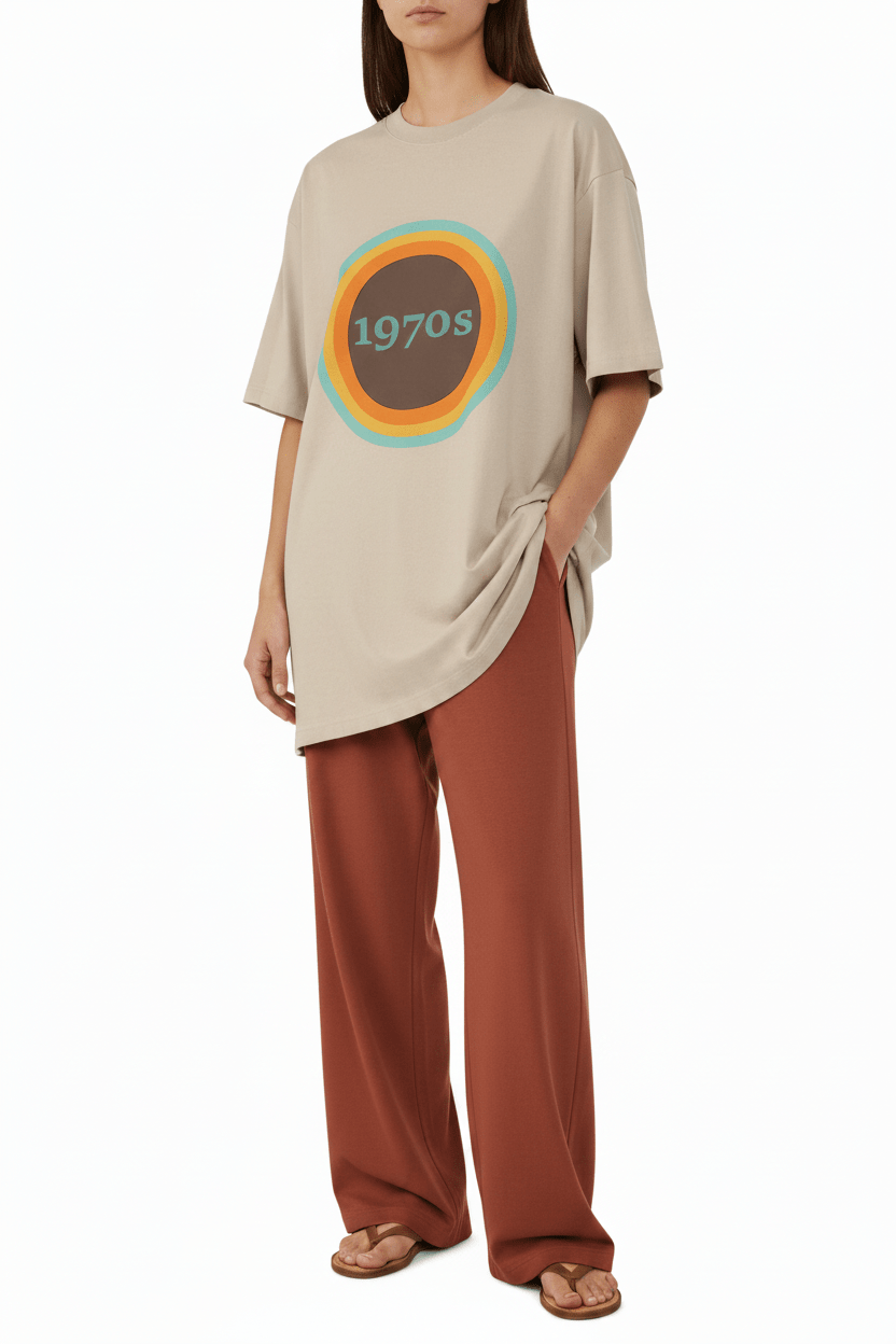 Woman wearing a beige oversized t-shirt with a graphic design and brown pants on a white background