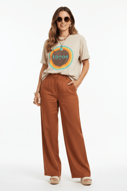 Woman wearing a beige t-shirt with a graphic design and brown pants on a white background