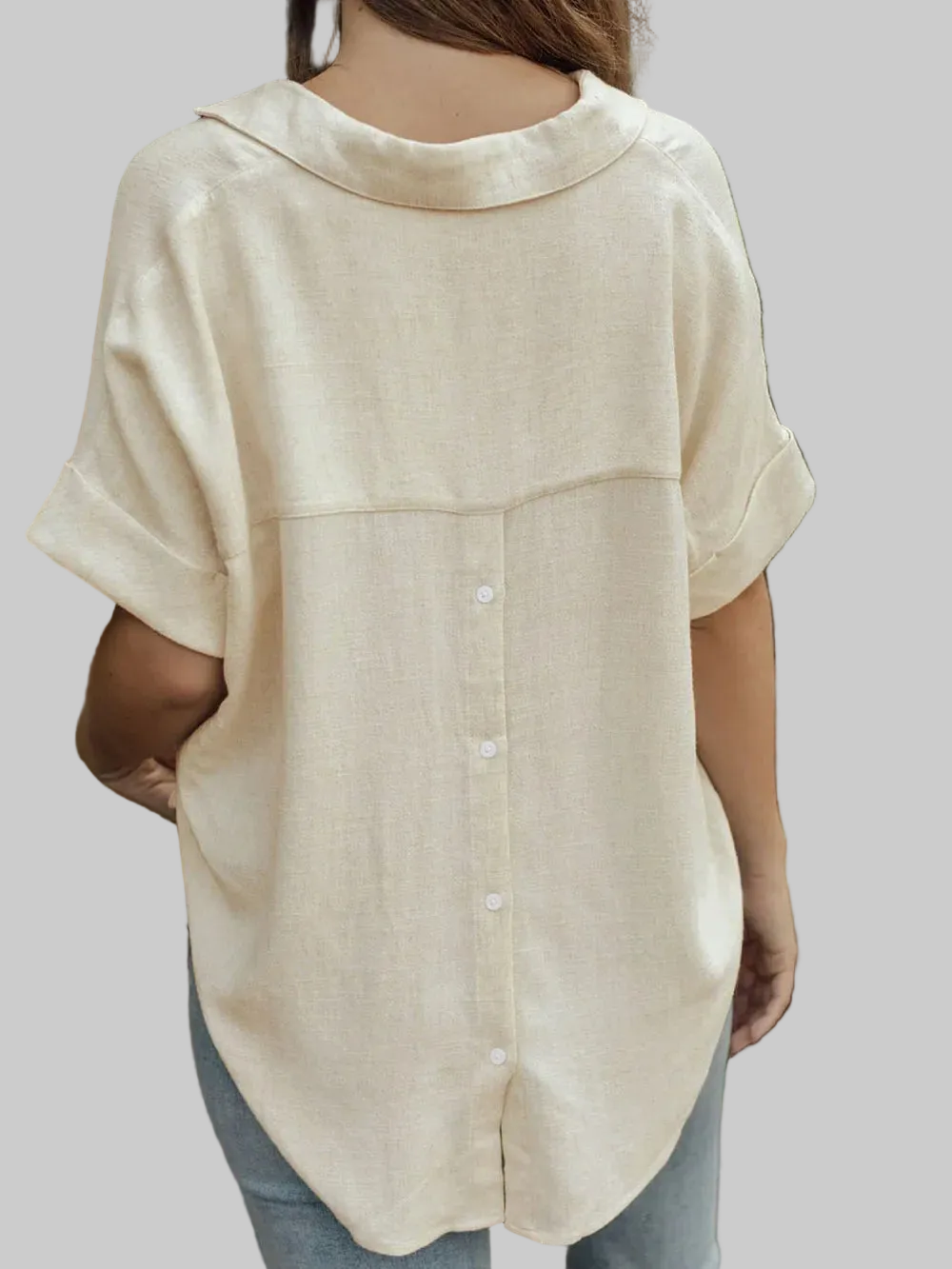 A woman wearing a light beige linen short-sleeve button-up shirt, shown from the back against a solid gray background.