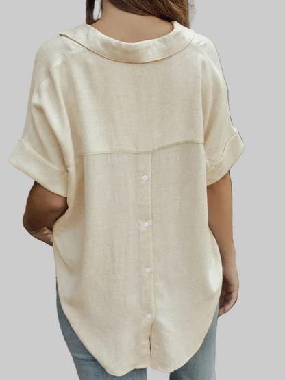 A woman wearing a light beige linen short-sleeve button-up shirt, shown from the back against a solid gray background.