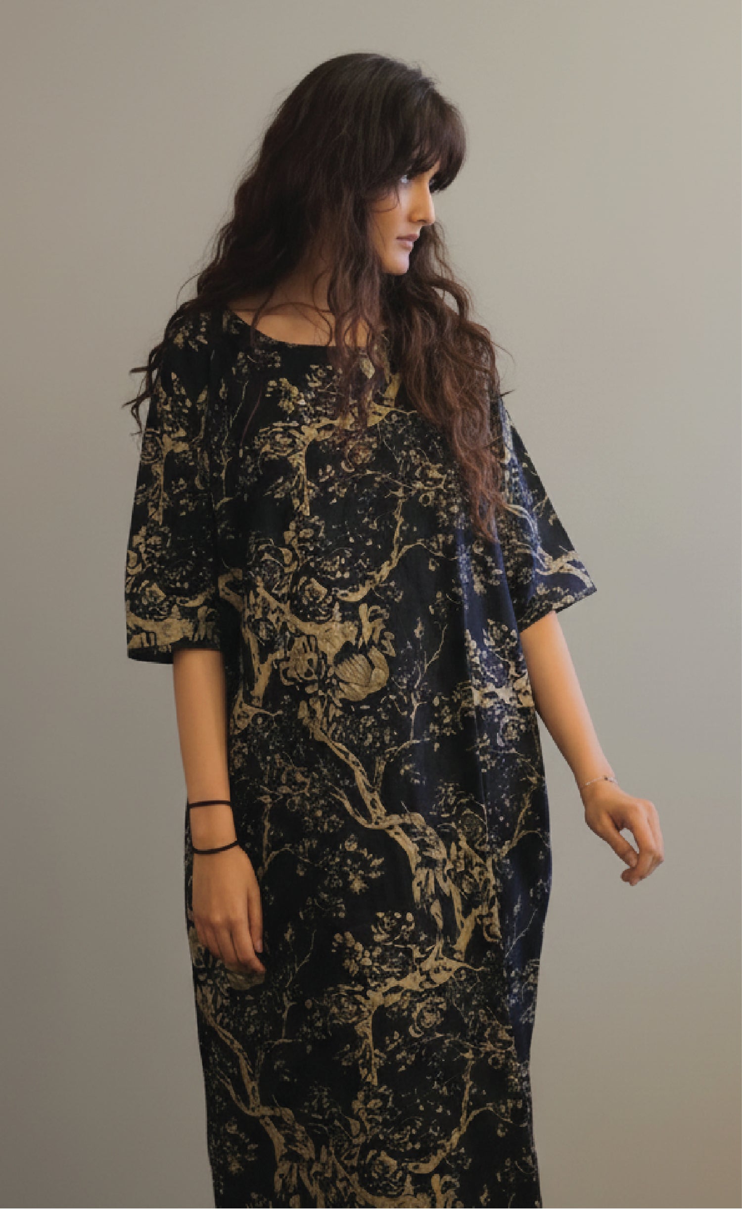 Woman wearing a black and gold patterned dress against a plain background