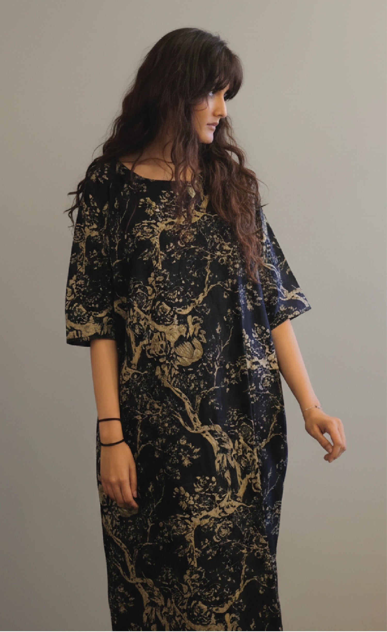 Woman wearing a black and gold patterned dress against a plain background