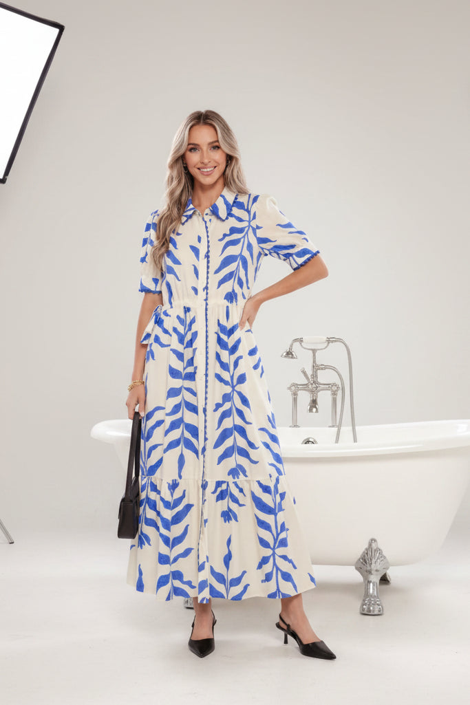 A woman wearing a blue and white patterned dress standing outdoors with plants in the background