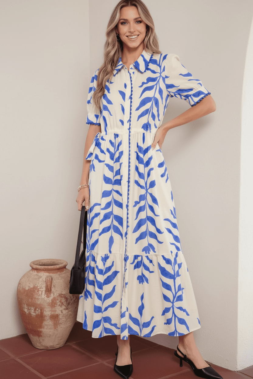 Woman wearing a white dress with blue leaf pattern standing next to a decorative vase.