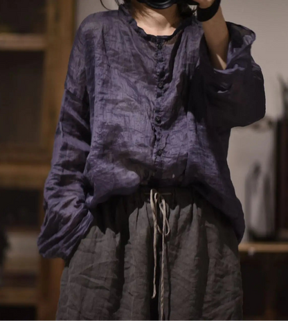 A person wearing a loose, dark purple textured long-sleeve top and dark gray drawstring pants in a dimly lit indoor setting.