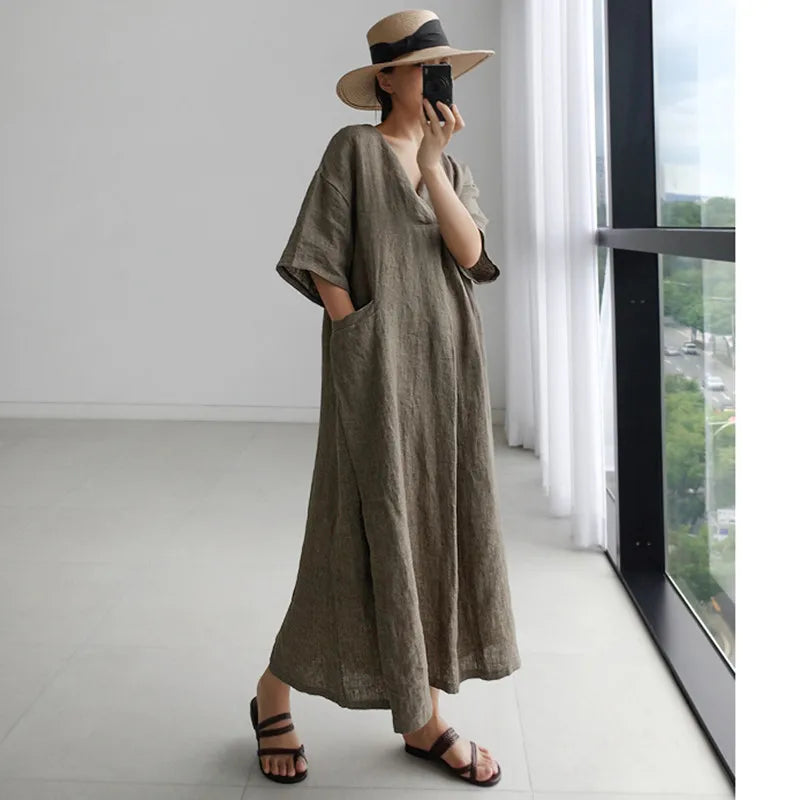 A woman is wearing a long baggy boho dress three quarter sleeves, v-neck with pockets.