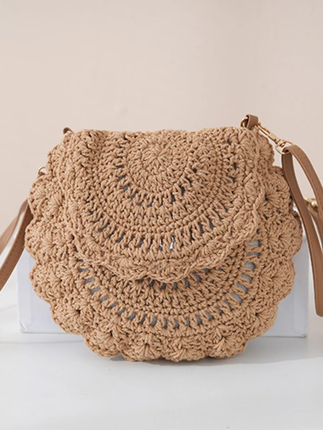 Brown crochet handbag on a white surface with a beige background