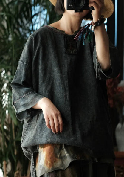 Person wearing a dark green oversized shirt taking a photo with a camera, surrounded by plants.