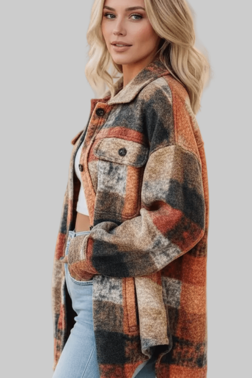 A woman wearing a chunky plaid button-up jacket in a warm autumn color palette of rust orange, brown, beige, and charcoal gray, paired with light blue jeans against a solid gray background.