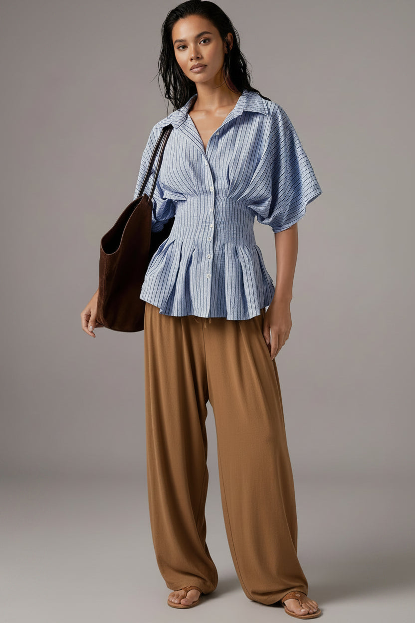 Woman wearing a blue striped shirt and shorts, holding a brown bag against a neutral background