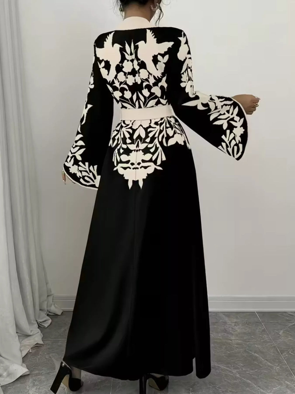Black dress with white floral patterns worn by a person, standing against a neutral background.