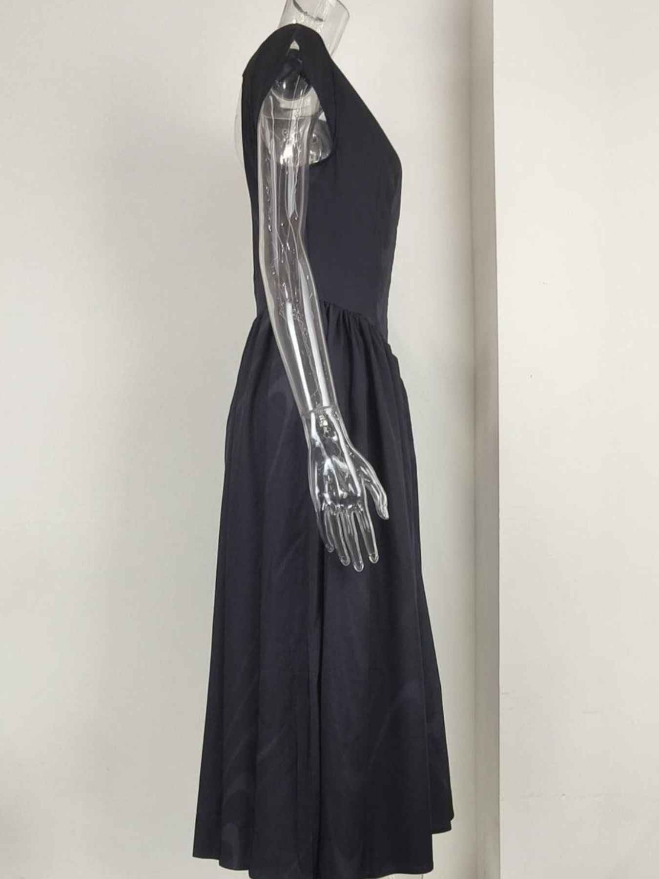 Black dress on a mannequin with a metallic arm against a white background