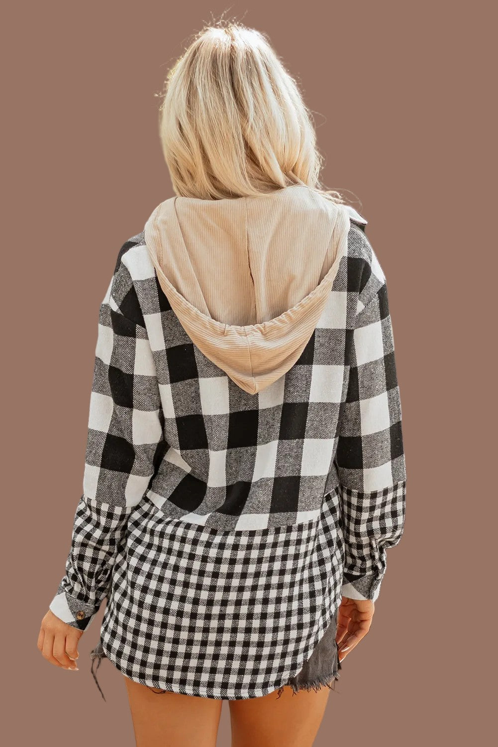 A woman viewed from the back wearing a black and white buffalo plaid hooded sweatshirt with a beige hood lining and matching plaid shorts, set against a solid brown background.