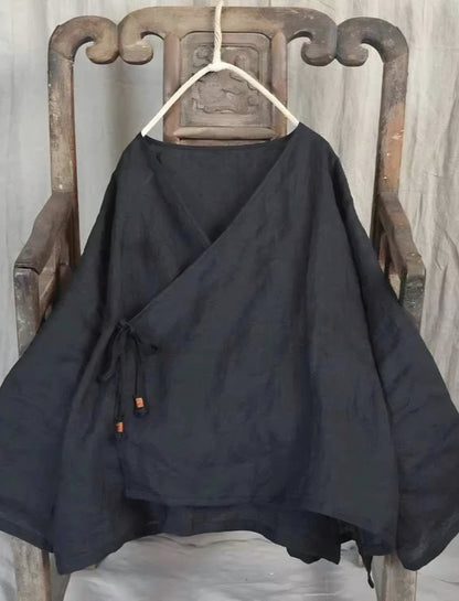 Black crossover top on a hanger against an old wooden chair and white wall.