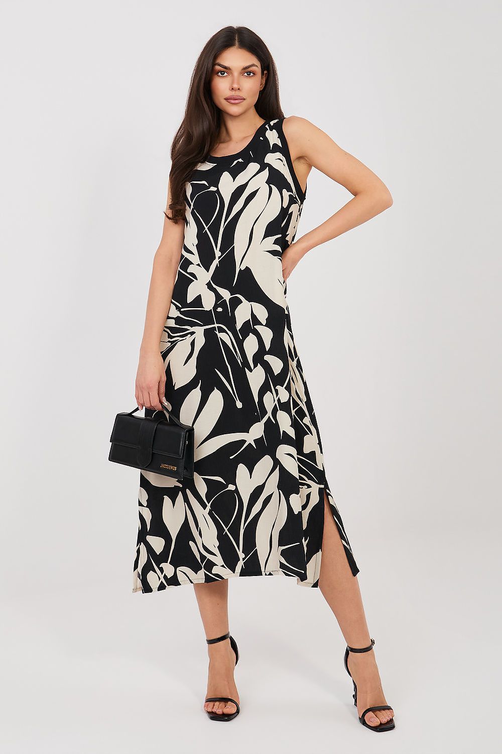 Sublevel sleeveless midi daydress in black botanical print viscose blend, round neck; model with black clutch.