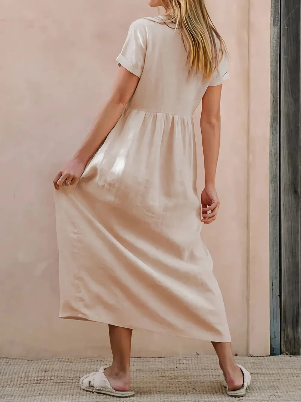 Woman wearing a long beige dress against a pink wall.