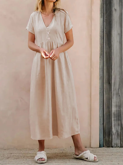 Woman wearing a beige dress is standing against a pink wall.
