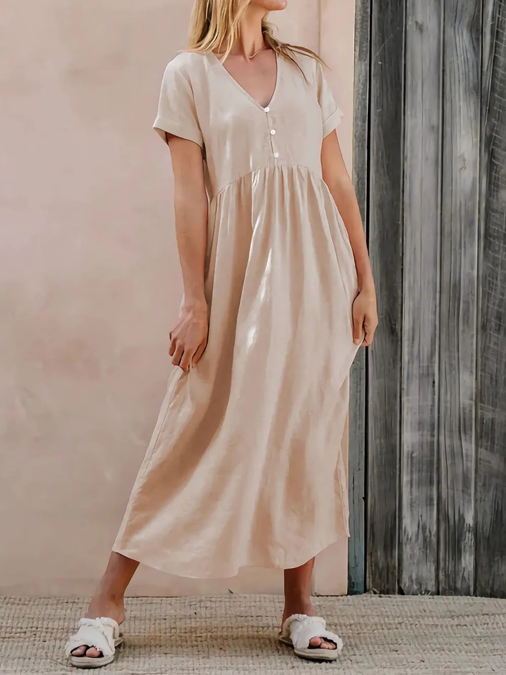 Woman wearing a beige dress is standing against a wooden wall.