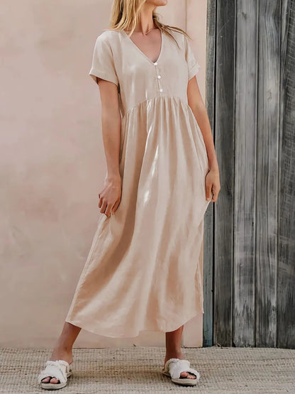 Woman wearing a beige dress is standing against a wooden wall.