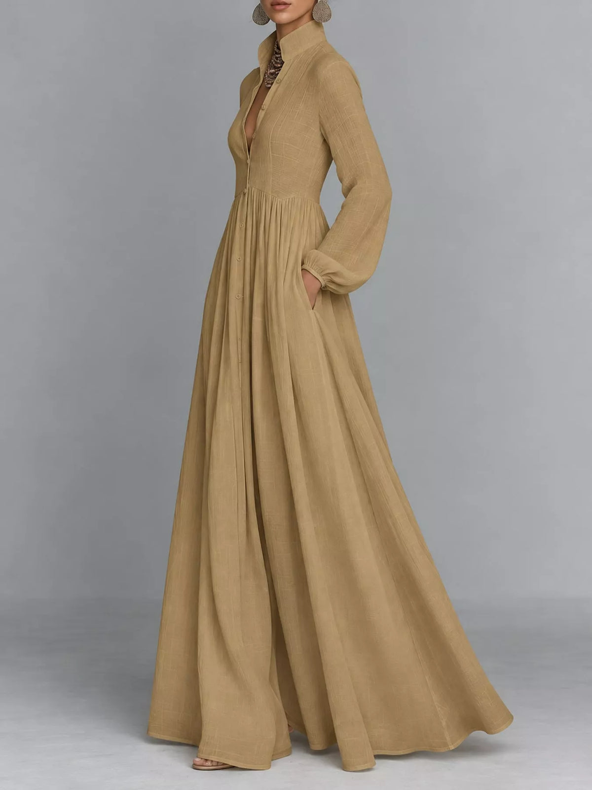 A woman models a long-sleeved, high-neck maxi dress in a warm camel tan color. The dress features a deep V-neckline, a gathered waist, and a flowing, wide-leg skirt with side pockets.