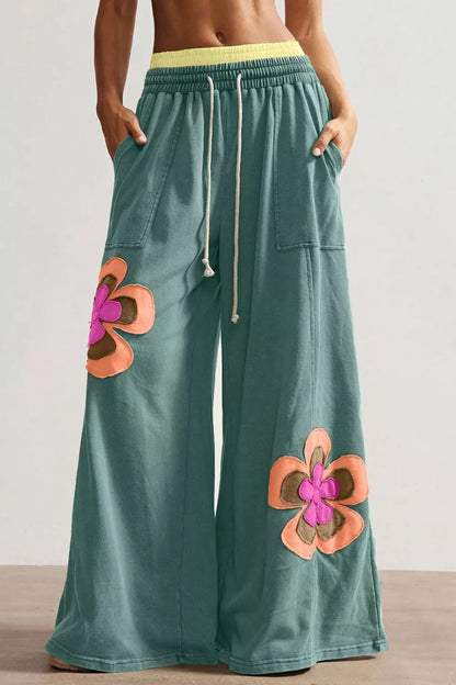 Green pants with floral patches worn by a person on a neutral background