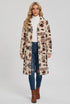 Woman wearing a long geometric pattern coat with pockets, paired with a white turtleneck and blue jeans.
