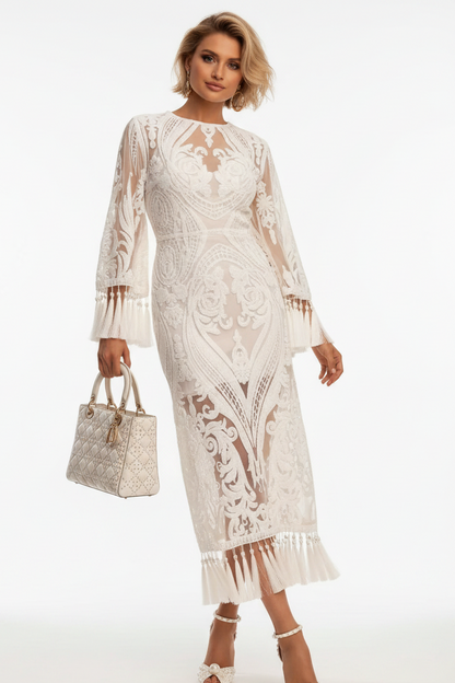 A woman models a long-sleeved cream lace midi dress with intricate floral embroidery and a fringed hem, holding a matching patterned handbag against a plain white studio background.
