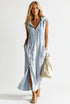 A woman wearing a light blue sleeveless midi dress with a front zipper, button-down front, and side pockets, standing outdoors next to a white picket fence and holding a beige tote bag.
