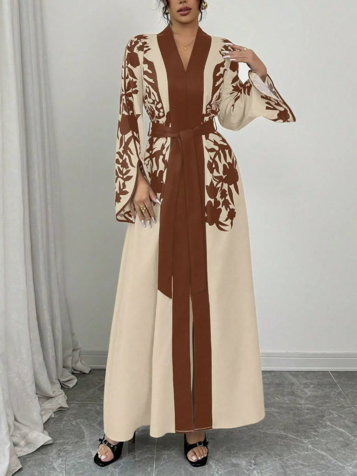 Woman wearing a long, patterned dress with a belt in a neutral setting