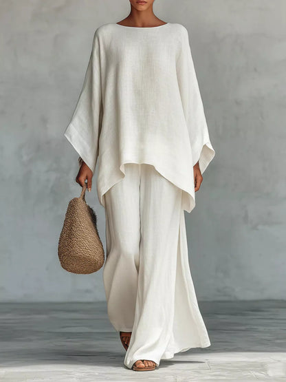 Person wearing a flowing white outfit holding a woven bag against a plain background