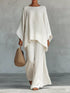 Person wearing a flowing white outfit holding a woven bag against a plain background