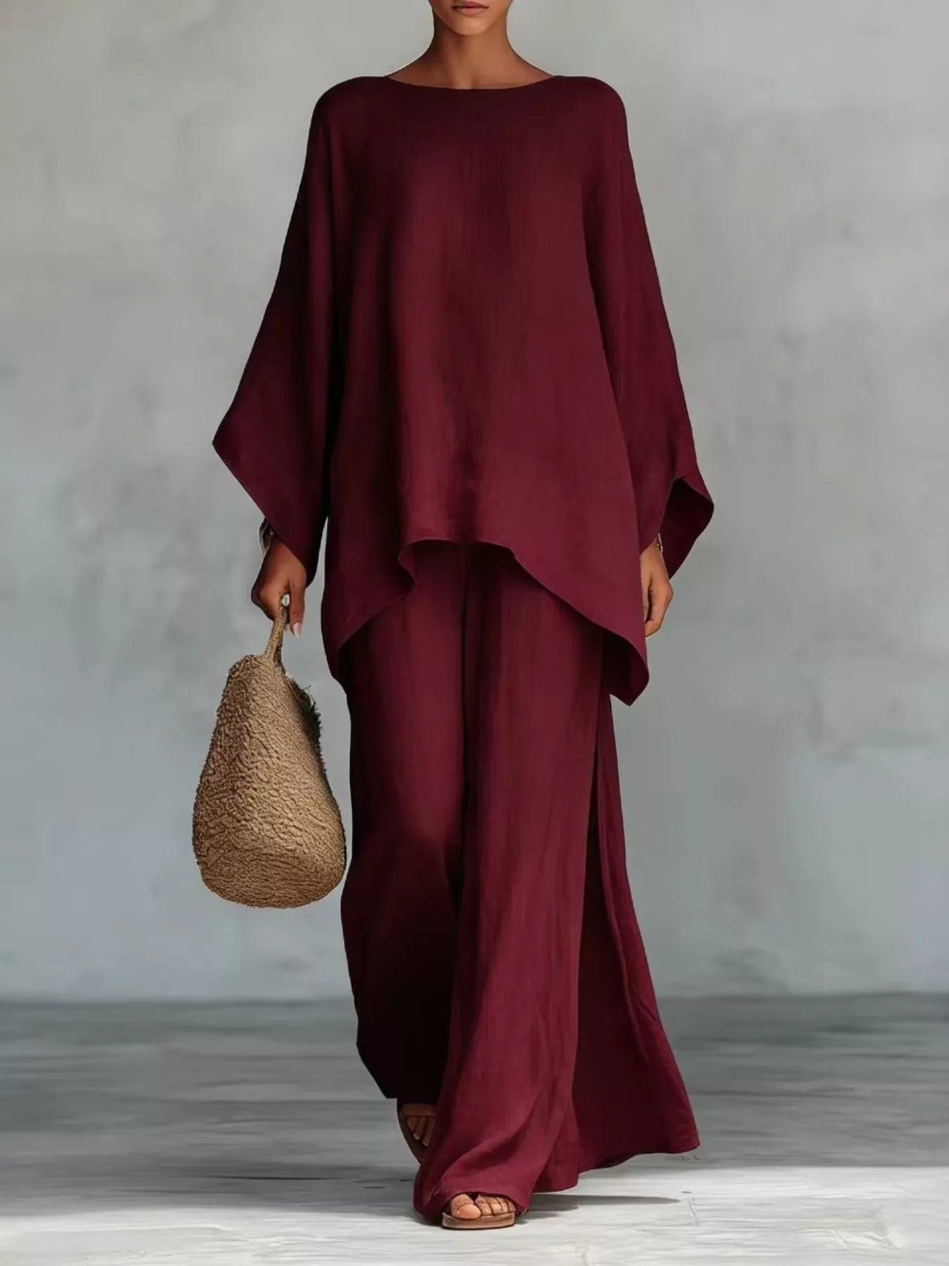 Person wearing a burgundy outfit holding a woven bag against a plain background