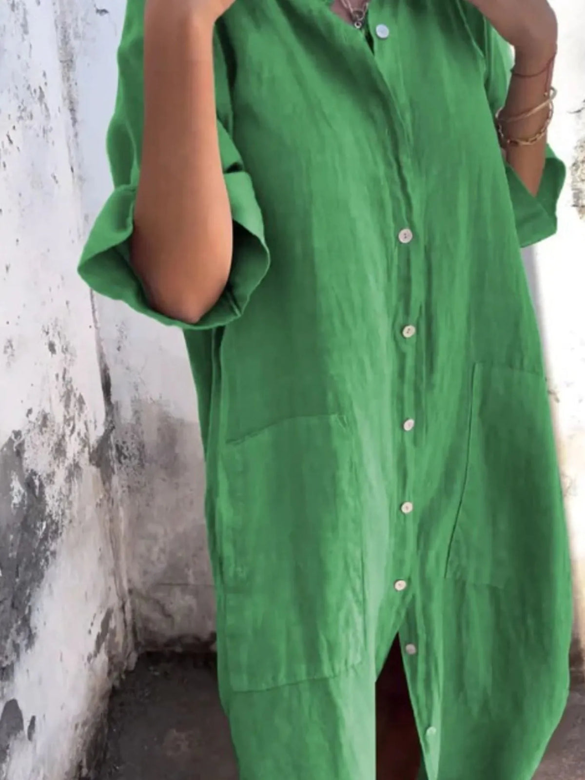 Person wearing a green dress with button details against a textured wall.