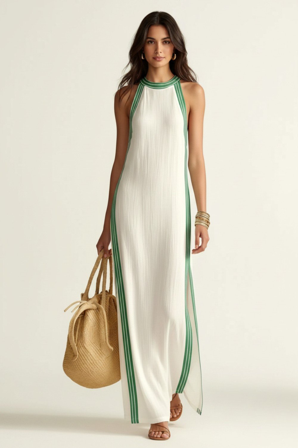 A woman modeling a sleeveless white maxi dress with green  side stripes and a green-trimmed neckline, holding a woven straw bucket bag against a plain light background.